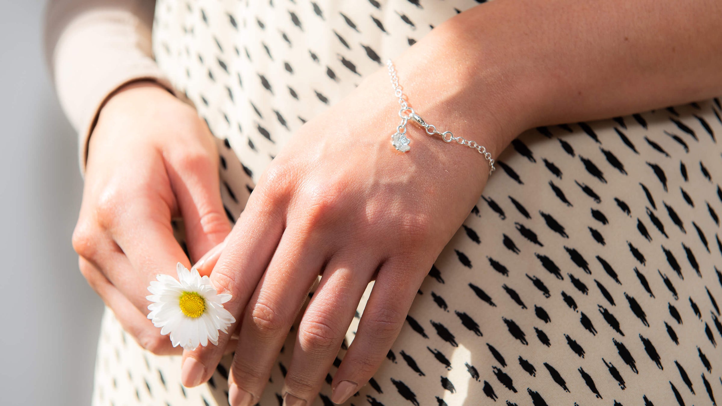 Model wearing Blackbird Jewellery’s handcrafted Primrose Bracelet, holding a delicate flower – inspired by nature