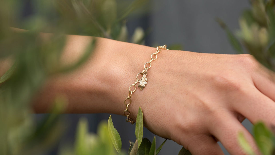 Gold vermeil oak leaf bracelet layered over a white shirt, styled for autumn. Handmade nature-inspired jewellery by Blackbird Jewellery.