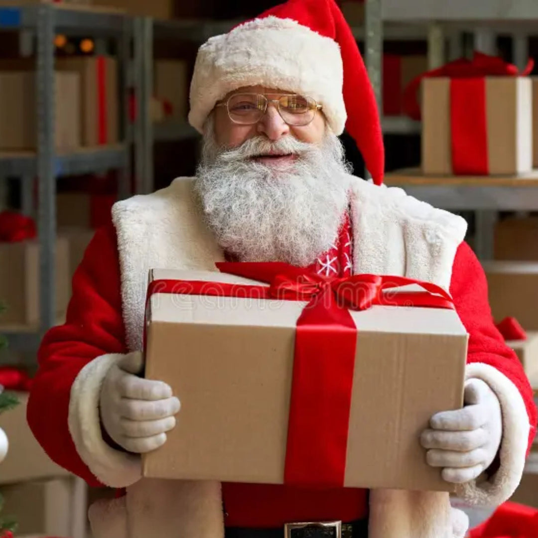 Santa Claus holding a large Christmas present with a red bow in a festive warehouse setting.