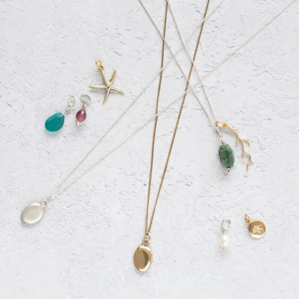 Handmade shell and pebble charm necklaces in gold vermeil and sterling silver from the Blackbird Jewellery Sea & Shore collection.