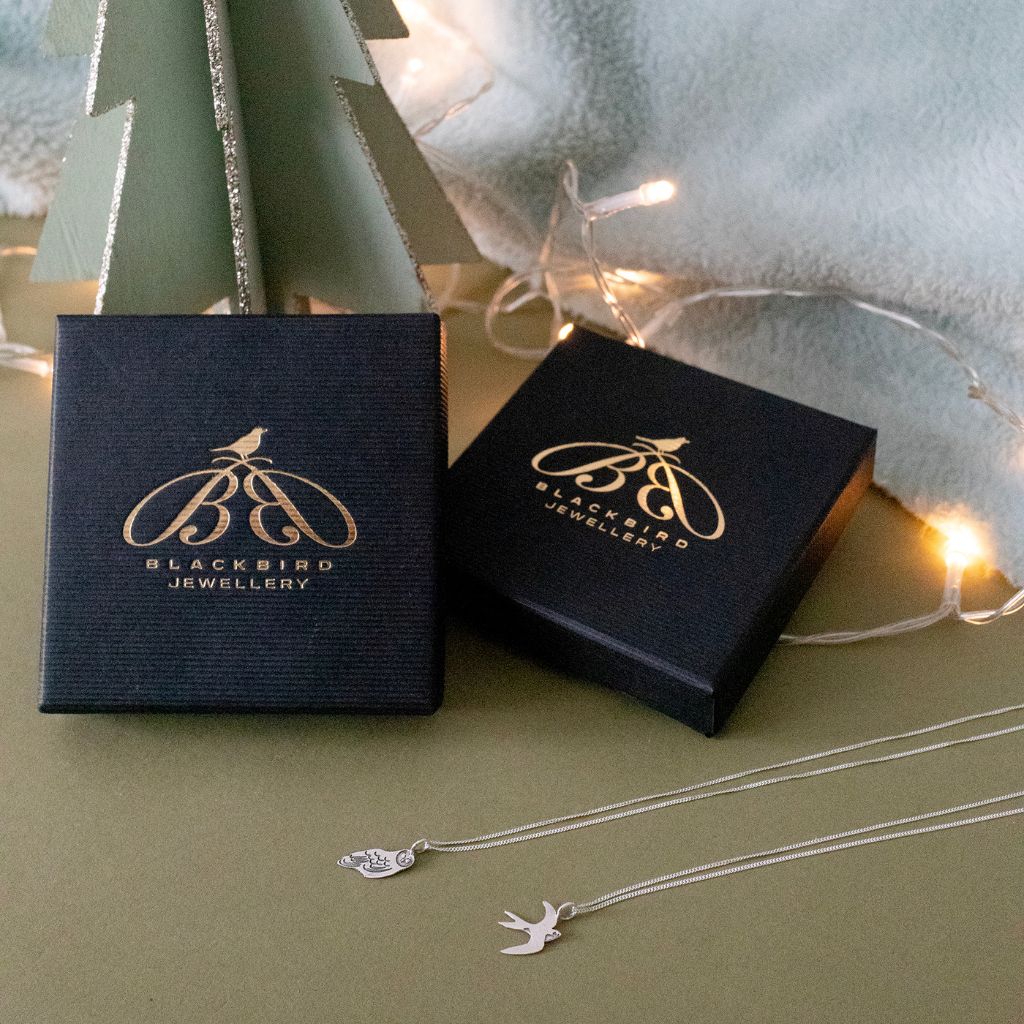 Blackbird Jewellery Christmas gifting display with sterling silver bird necklaces and branded gift boxes beneath a small green tree with fairy lights.