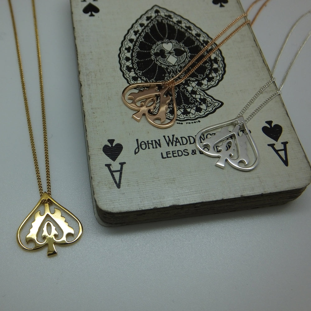 Two necklaces with heart and spade pendants on a playing card with 'John Waddell Leeds & Co' branding.