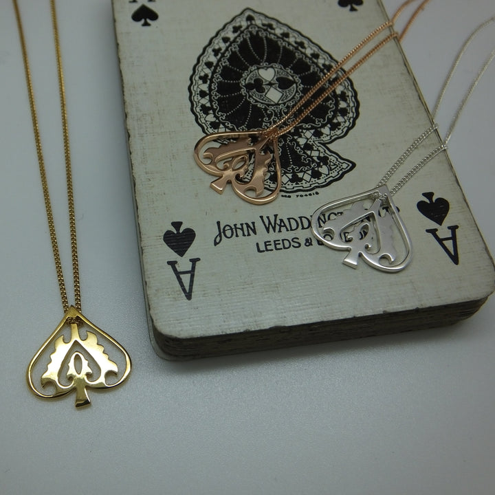 Two necklaces with heart and spade pendants on a playing card with 'John Waddell Leeds & Co' branding.
