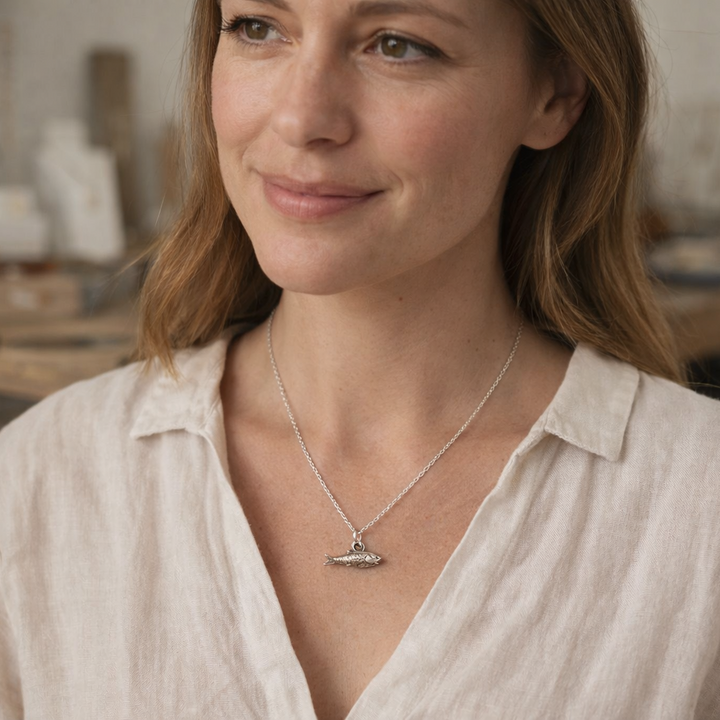 woman wearing sterling silver lucky fish charm necklace with fine chain, handcrafted fish pendant inspired by ocean symbolism and good luck jewellery