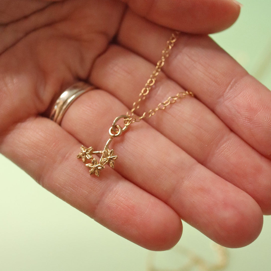 Blackbird Jewellery 18ct Gold forget me not sprig necklace held in a hand against a light green background
