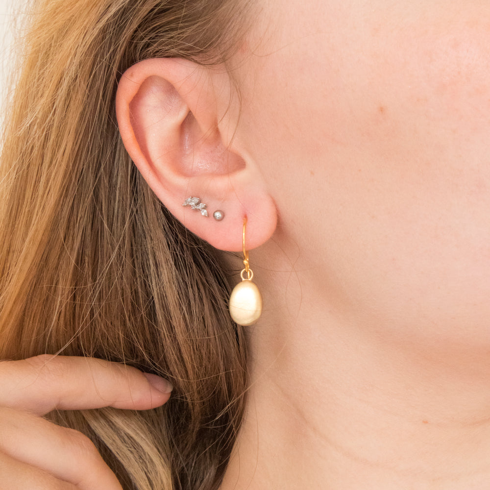 Model wearing 18ct gold vermeil pebble drop earrings with soft golden shine.