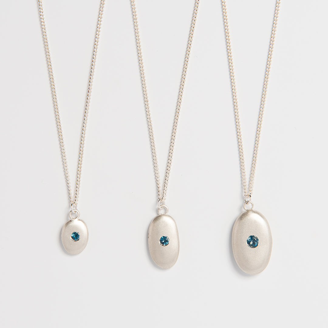 Close-up detail of handcrafted silver pebble pendant with blue topaz centre.
