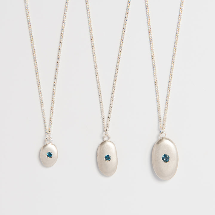 Close-up detail of handcrafted silver pebble pendant with blue topaz centre.