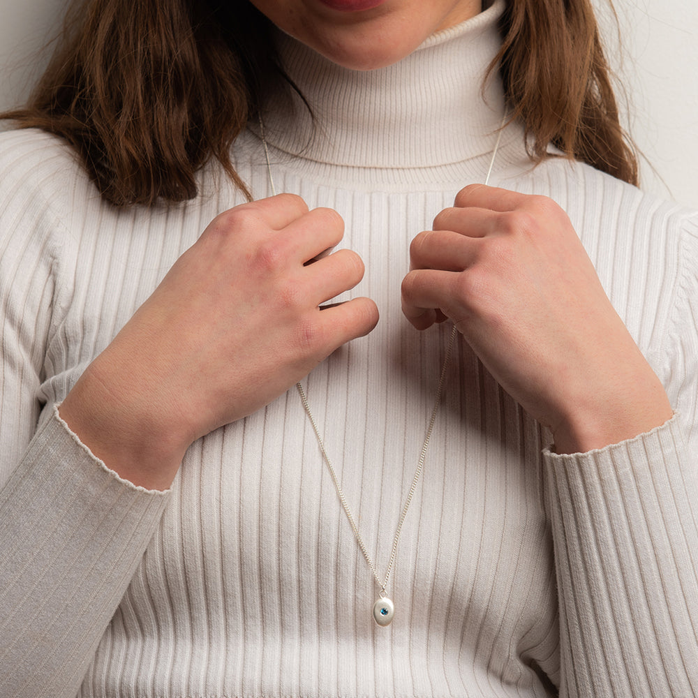 Model wearing small sterling silver pebble necklace with blue topaz, layered style.
