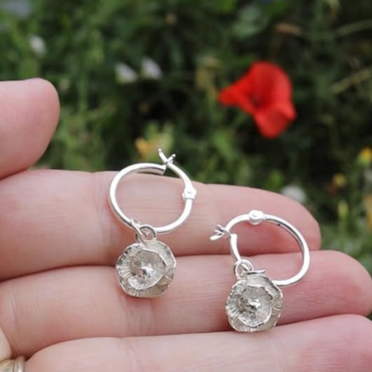 Blackbird Jewellery Poppy Silver hoop earrings held between fingers with a blurred natural background