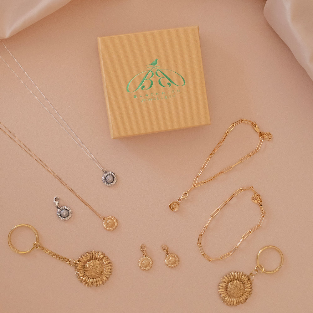 Sunflower jewellery set by Blackbird Jewellery featuring handmade necklaces, earrings, charms, and keyrings in sterling silver and 18ct gold vermeil with gift box on soft neutral background.