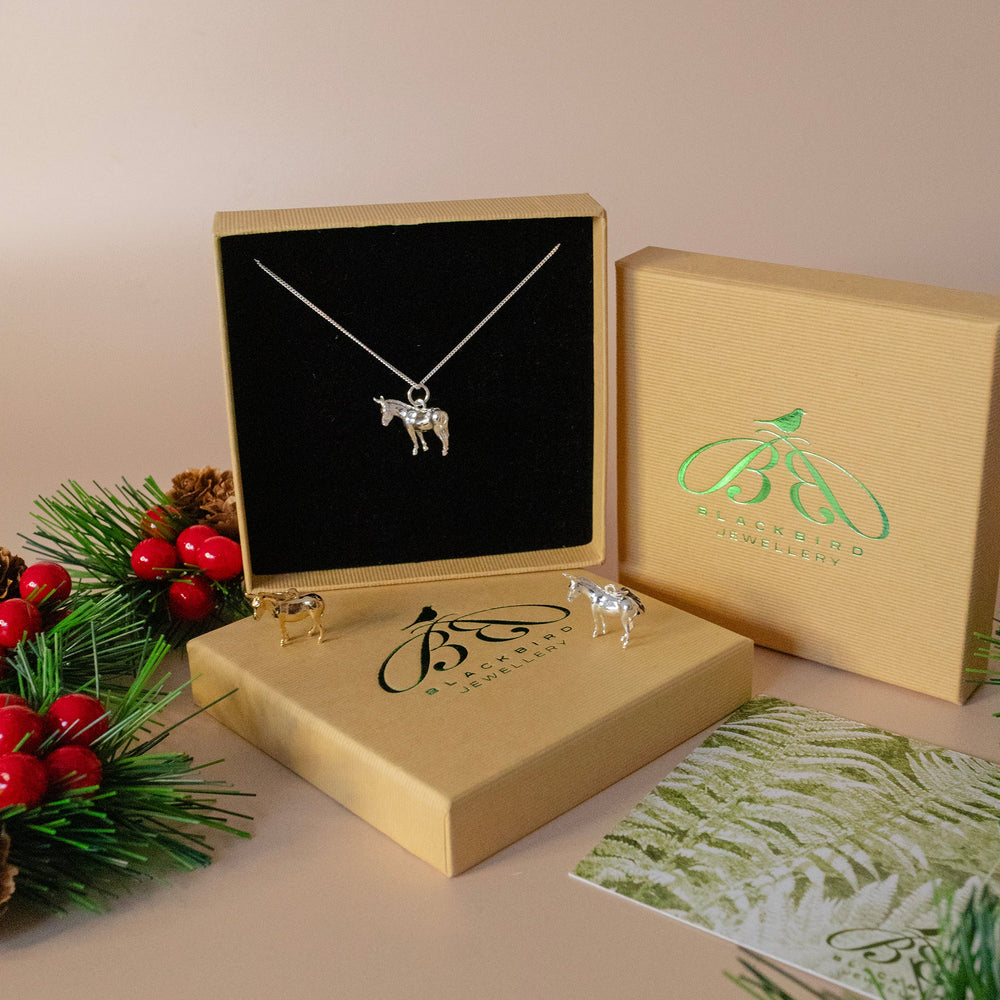 Silver donkey necklace in a jewelry box with a Christmas-themed card and decorations.