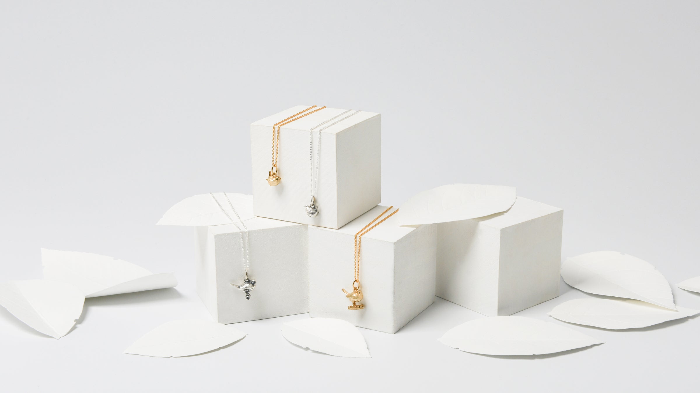 Blackbird Jewellery sterling silver and gold vermeil bird necklaces displayed on stacked white gift boxes with paper leaves in a soft, nature-inspired setting.