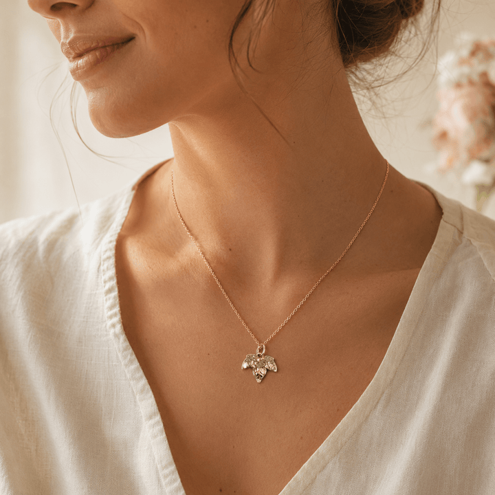 A close-up lifestyle shot of a woman wearing a delicate gold chain ivy necklace with a small gold ivy pendant, styled with a white V-neck top.