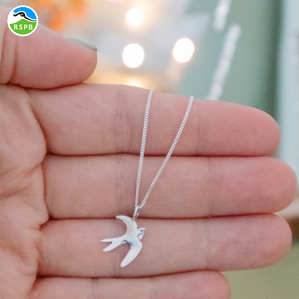 Blackbird Jewellery a sterling silver swallow pendant necklace held in a person's hand, with the pendant in the shape of a bird in flight.