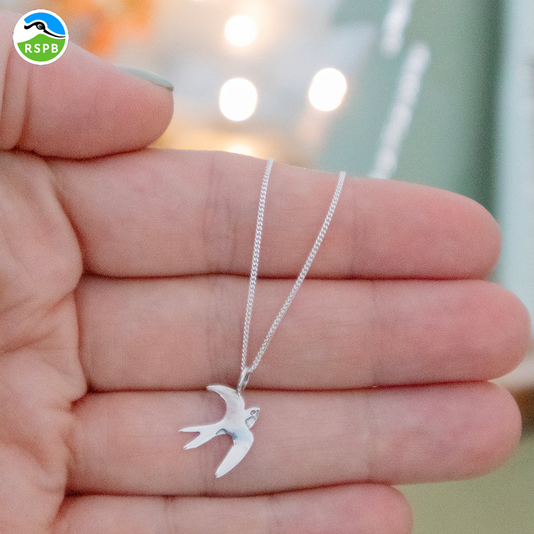Blackbird Jewellery a sterling silver swallow pendant necklace held in a person's hand, with the pendant in the shape of a bird in flight.