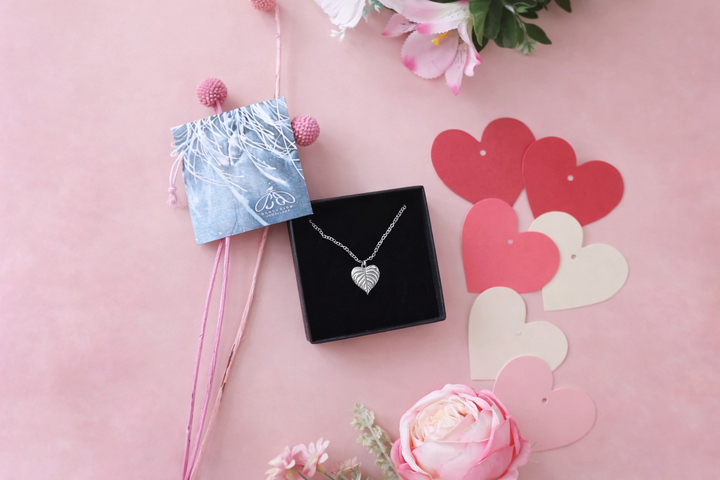 Heart-shaped necklace in a black box with pink flowers and heart decorations on a pink background