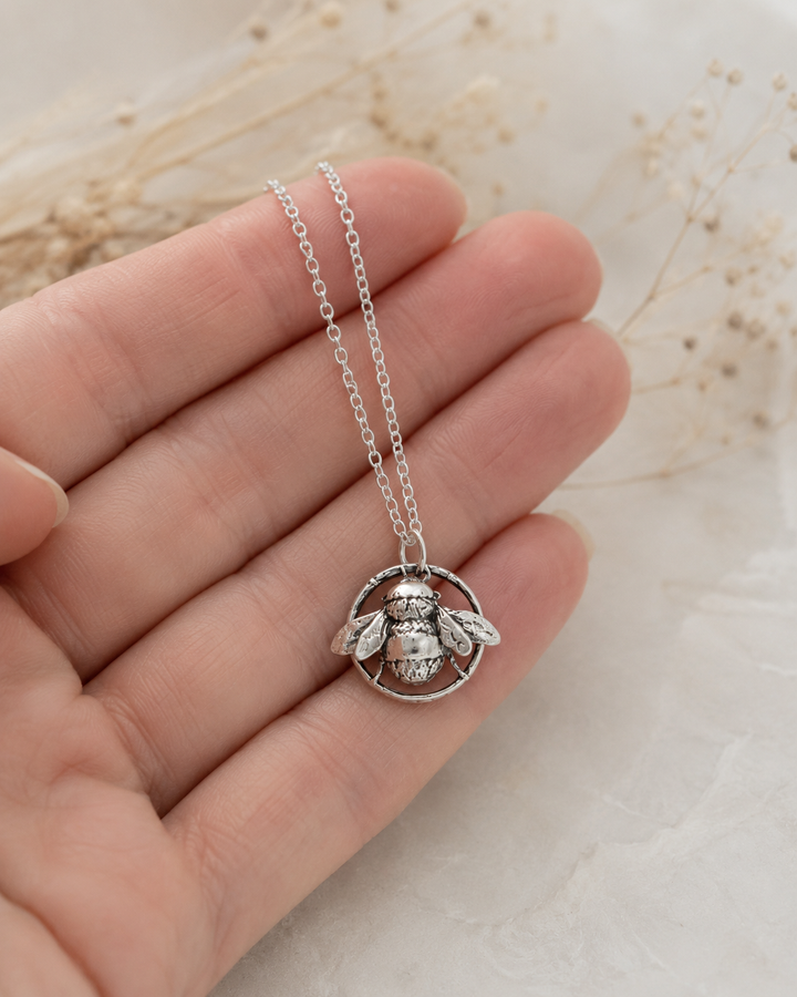Sterling silver bee pendant necklace held gently in hand, showing the detailed bee charm and delicate chain