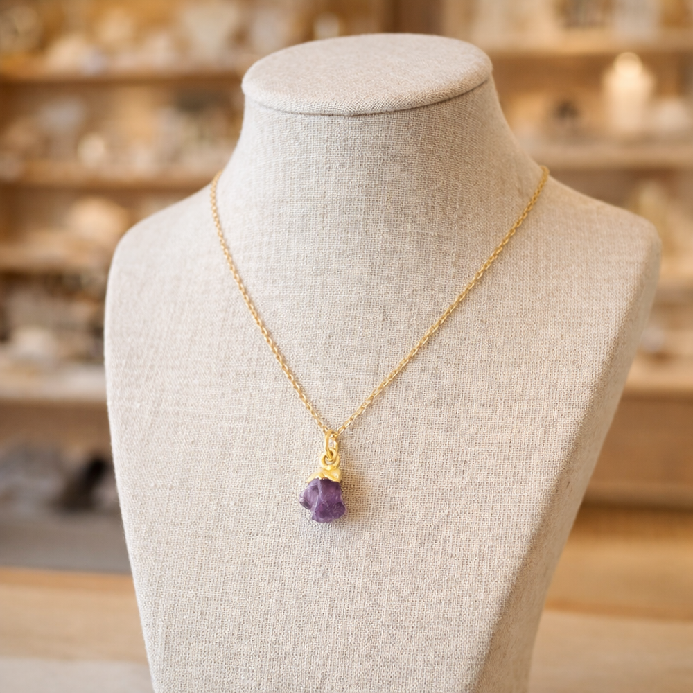 Gold vermeil raw amethyst crystal necklace displayed on a cream linen bust mannequin inside the Blackbird Jewellery shop with a softly blurred boutique background