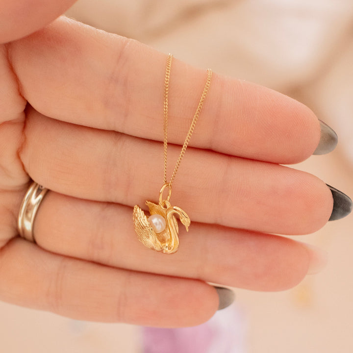 Blackbird Jewellery Gold necklace with a swan pendant held between fingers against a neutral background