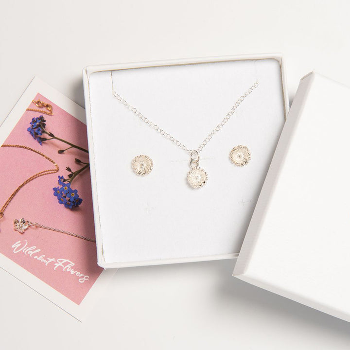 Blackbird Jewellery silver daisy necklace and earring jewellery set, presented in a white box with a floral motif. The set features a daisy design on the necklace and earrings, symbolizing the birth flower for April.