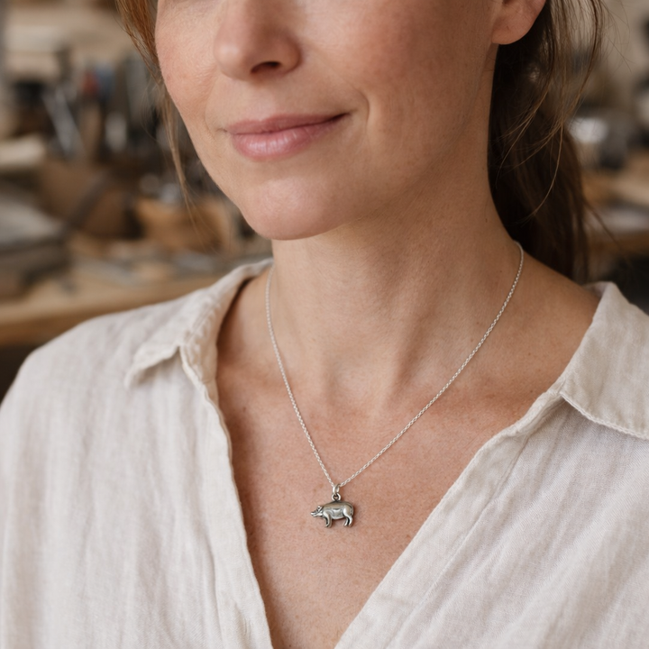 Blackbird Jewellery Woman wearing a sterling silver pig charm necklace on a fine chain, styled in a natural jewellery studio setting with soft lighting