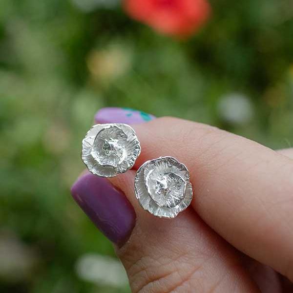 Blackbird Jewellery sterling silver poppy stud earrings held in hand, handmade remembrance jewellery inspired by nature