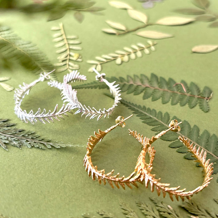 Two pairs of hoop earrings, one gold and one silver, on a green leafy background.
