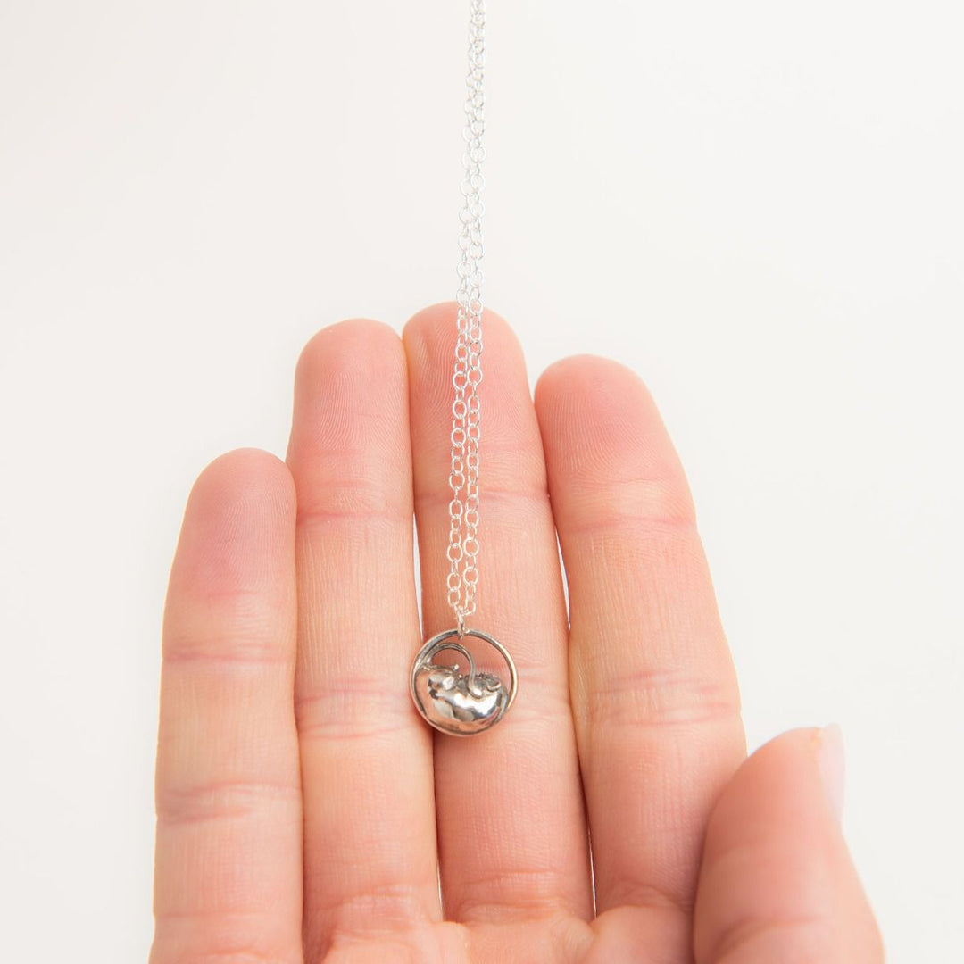 Close-up of the sterling silver sleeping dormouse necklace resting in a hand, showing the delicate size and detailing.